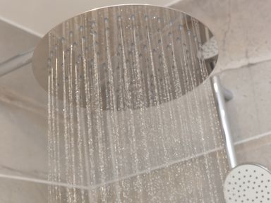 Water flowing from a round overhead shower head in a bathroom at Sea Sands in Praa Sands