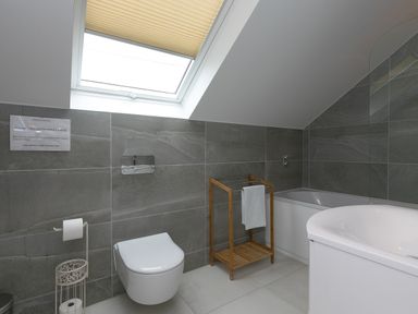 A bathroom with a wall-mounted toilet wooden towel rack bathtub and skylight window at Sea Sands in Praa Sands