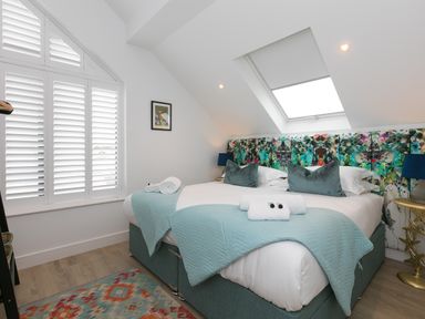 A bedroom with a double bed blue bedding a skylight window and white shutters at Sea Sands in Praa Sands