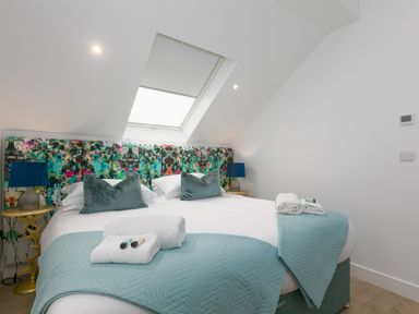 A bedroom with a large bed under a skylight featuring colorful headboard and bedside tables with lamps at Sea Sands in Praa Sands