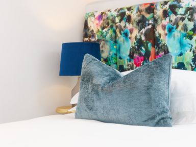 A bed with a blue pillow and a colorful floral headboard with a blue lamp on a bedside table at Sea Sands in Praa Sands