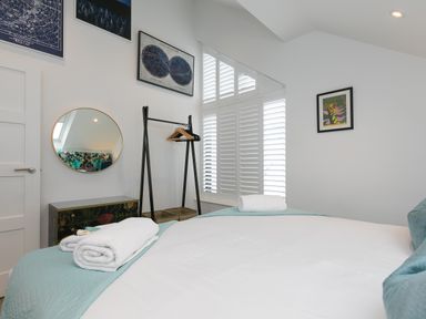 A bedroom with a bed with towels a black freestanding clothes rack a round mirror and framed pictures at Sea Sands in Praa Sands