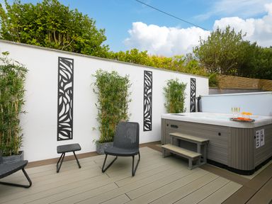 An outdoor patio with a hot tub chairs small table plants and decorative wall panels at Sea Sands in Praa Sands