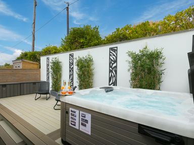 An outdoor patio with a hot tub champagne glasses two chairs plants and decorative wall panels at Sea Sands in Praa Sands