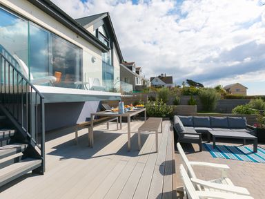 An outdoor deck with table and benches and a seating area with a sofa and armchairs at Sea Sands in Praa Sands
