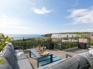 An outdoor patio with gray sofas and a table set with drinks and snacks overlooking the sea at Sea Sands in Praa Sands