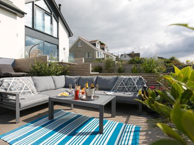 An outdoor seating area with a grey sectional sofa and a table with drinks and snacks at Sea Sands in Praa Sands