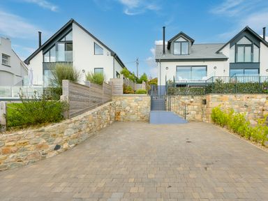 A paved driveway with stone walls leading to modern houses with large windows and balconies at Sea Sands in Praa Sands