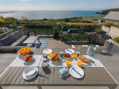 A patio dining table set for breakfast with croissants strawberries orange juice and fruit overlooking the sea at Sea Sands in Praa Sands