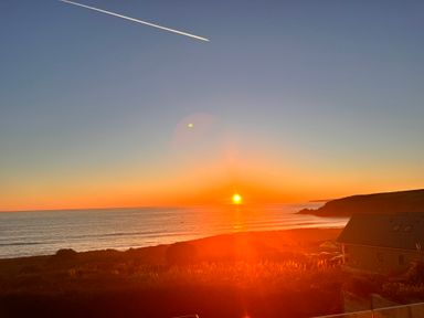 A sunset over the ocean with cliffs and a house near the shore at Sea Sands in Praa Sands