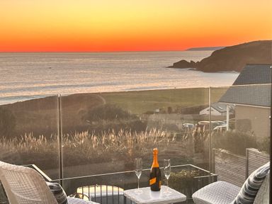A balcony with two chairs and a table with a bottle and glasses overlooking the ocean at Sea Sands in Praa Sands