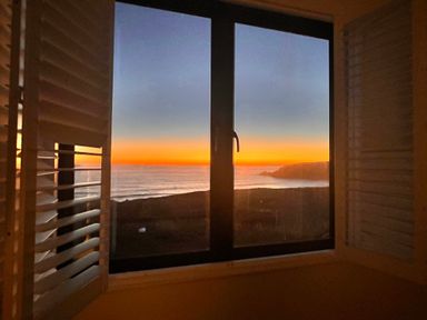 A window with shutters open showing an ocean view at sunset at Sea Sands in Praa Sands