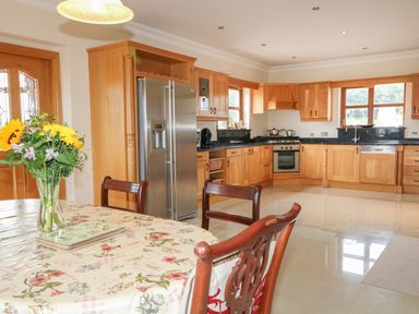 A kitchen with wooden cabinets and a stainless steel refrigerator with a table and chairs and flowers in a vase at Redford View in Culdaff County Donegal