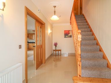 An entry hallway with a wooden staircase carpeted stairs a small table with flowers and a painting on the wall at Redford View Culdaff County Donegal