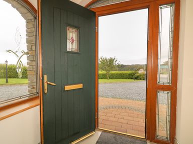 An open front door with stained glass panels beside a window showing a garden driveway and lawn at Redford View in Culdaff County Donegal