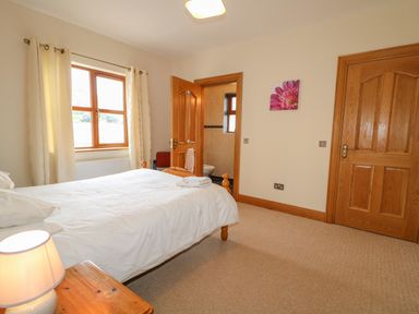 A bedroom with a bed a wooden side table with a lamp a window with curtains two wooden doors and a wall picture at Redford View in Culdaff County Donegal
