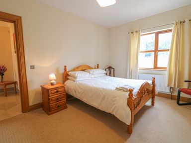 A bedroom with a wooden bed with white bedding a nightstand with a lamp a window with curtains and a chair at Redford View in Culdaff County Donegal