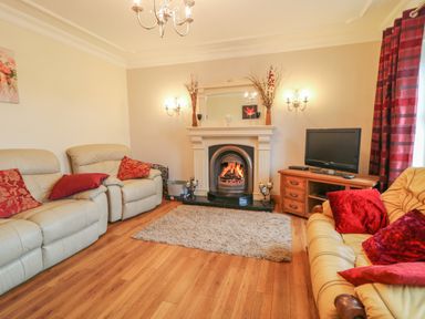 A living room with beige sofas red cushions a fireplace a television on a wooden stand and red curtains at Redford View in Culdaff County Donegal