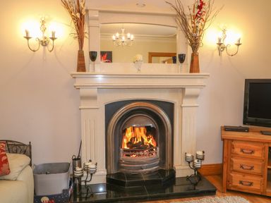 A fireplace with a fire burning a large mirror above and wall lamps on each side at Redford View in Culdaff County Donegal