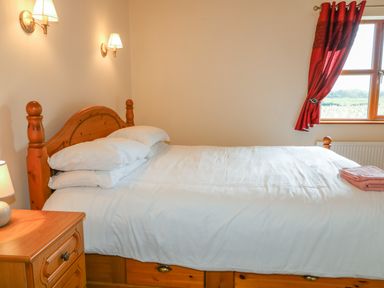 A bedroom with a wooden bed a bedside table with a lamp and red curtains at Redford View Culdaff County Donegal