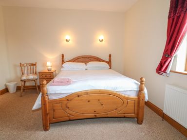 A bedroom with a wooden bed and white bedding a chair bedside table with lamp and red curtains at Redford View in Culdaff County Donegal