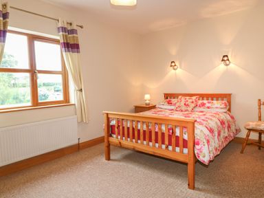 A bedroom with a wooden bed floral bedding bedside table with lamp chair and window at Redford View in Culdaff County Donegal