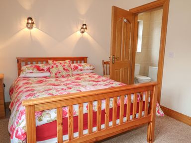 A bedroom with a wooden bed frame floral bedding wall lights and an open door leading to a bathroom at Redford View in Culdaff County Donegal