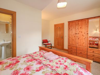 A bedroom with floral bedding wooden wardrobe a red chair and a door leading to a bathroom at Redford View in Culdaff County Donegal