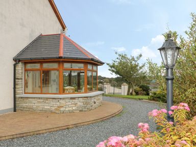 A patio area with a stone and wood conservatory window and a garden path with a lamp post and flowers at Redford View in Culdaff County Donegal