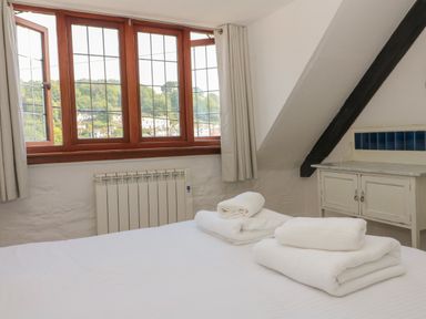 A bedroom with a bed and folded towels near a window and a white cabinet at Pixie Cottage in Looe