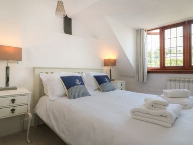 A bedroom with a double bed two bedside tables with lamps and folded towels on the bed at Pixie Cottage in Looe