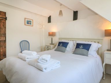 A bedroom with a double bed white bedding and blue nautical pillows two nightstands with lamps a blue chair and folded towels on the bed at Pixie Cottage in Looe