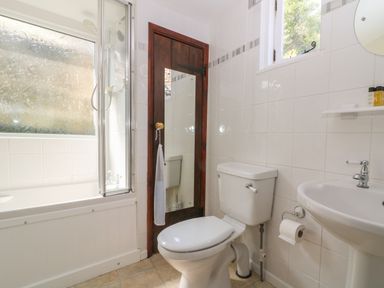 A bathroom with a toilet sink and bathtub with glass shower screen at Pixie Cottage in Looe