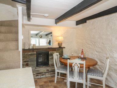 A dining area with a round wooden table and four chairs near a stone fireplace and stairs at Pixie Cottage in Looe