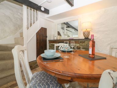 A dining area with a round wooden table set with dishes and wine glasses near carpeted stairs at Pixie Cottage in Looe