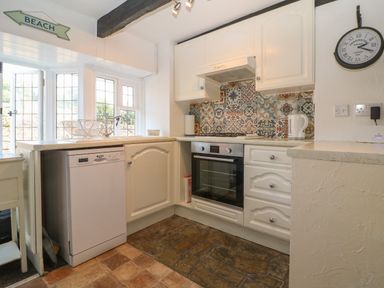 A kitchen with white cabinets a dishwasher an oven and a tiled backsplash at Pixie Cottage in Looe