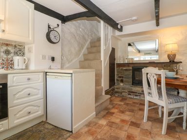 A kitchen and dining area with a small fridge stairs and a dining table with chairs at Pixie Cottage in Looe