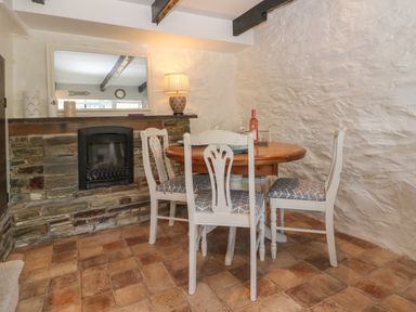 A dining area with a round wooden table and four chairs beside a stone fireplace with a mirror on top at Pixie Cottage in Looe