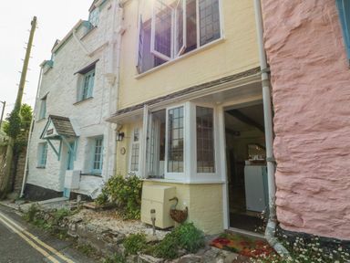 Exterior view of pastel colored cottages with open windows and plants along a narrow street at Pixie Cottage in Looe