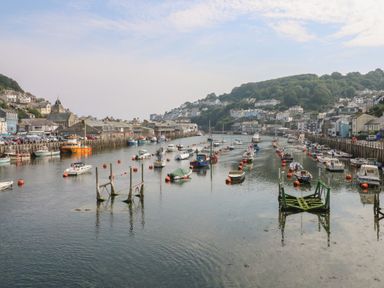 A harbor with boats moored along the sides and on the water with buildings and hills in the background at Pixie Cottage in Looe