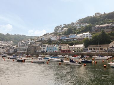 A harbor with boats moored on the water and houses on a hillside at Pixie Cottage in Looe