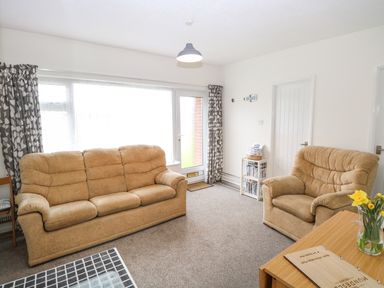 A living room with two beige sofas a small side table with books and a wooden table with flowers at 14 Siesta Mar in Mundesley
