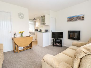 A living room with sofas a wall-mounted fireplace a TV and a drop-leaf dining table next to a kitchen at 14 Siesta Mar in Mundesley