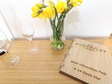 A wooden table with yellow flowers in a glass vase two empty wine glasses and a guest information pack at 14 Siesta Mar in Mundesley