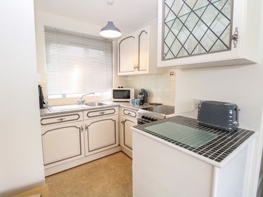 A kitchen with white cabinets a toaster microwave kettle a sink and a window with blinds at 14 Siesta Mar in Mundesley