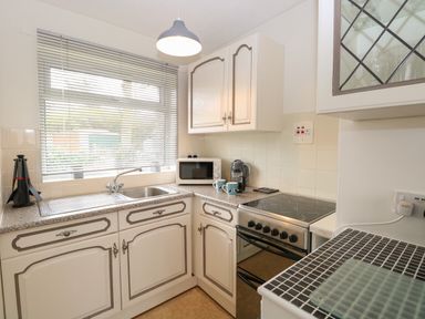 A kitchen with white cabinets a stove a microwave and a window with blinds at 14 Siesta Mar in Mundesley