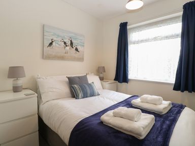 A bedroom with a bed with folded towels bedside tables lamps and a window with blue curtains at 14 Siesta Mar in Mundesley