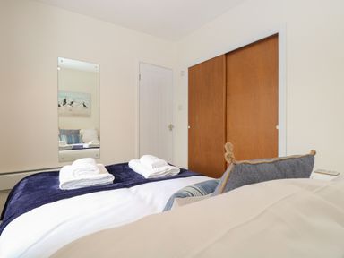 A bedroom with a bed covered in white and blue bedding towels on the bed a mirror on the wall a door and wooden sliding closet doors at 14 Siesta Mar in Mundesley