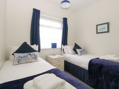 A bedroom with two single beds a nightstand and a window with curtains at 14 Siesta Mar in Mundesley