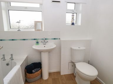 A bathroom with a bathtub sink toilet windows and a basket with towels at 14 Siesta Mar in Mundesley